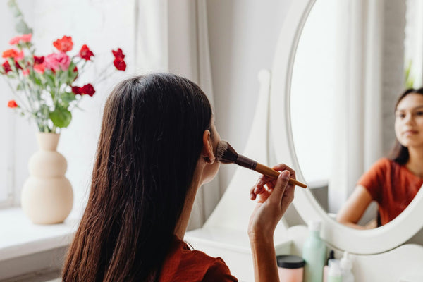  A woman sits at a vanity table with mirror and puts on makeup – Modern Mirrors